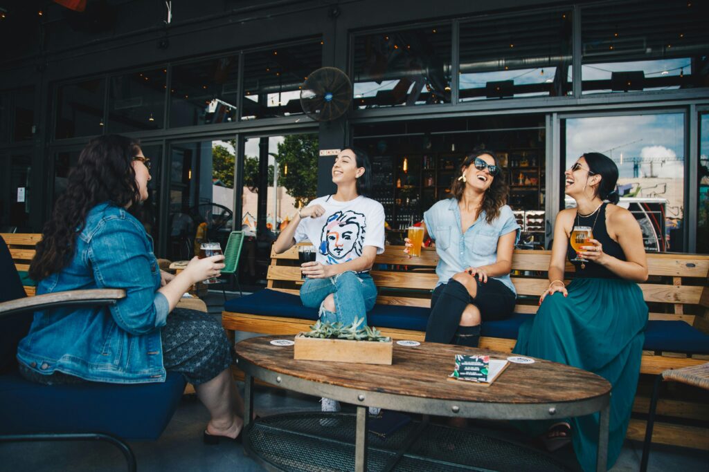 Four friends laughing and enjoying drinks together at an outdoor cafe setting, reflecting happiness and camaraderie.